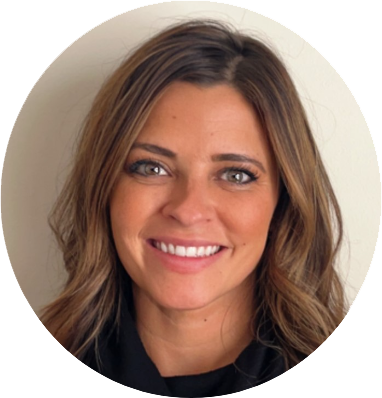 The image is a headshot of a woman with a bright and inviting smile. She has medium-length hair with highlights ranging from brunette to blond, styled with a slight wave. Her complexion is tan, and her makeup is done in a way that accentuates her features, including defined eyebrows, mascara, and a glossy pink lipstick. She is wearing a black top, which provides a stark contrast to her light hair and adds to the professional look of the image. The background is neutral, ensuring that the focus remains on her. The lighting in the image is well-balanced, with a soft glow on her face that enhances her friendly and confident expression.