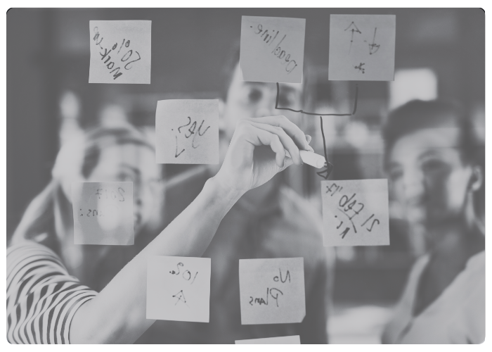 blurry people drawing on sticky notes attached to a clear board